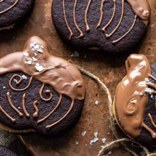 Chocolate sandwich cookies topped with milk chocolate drizzle and sea salt, set on a wooden surface.