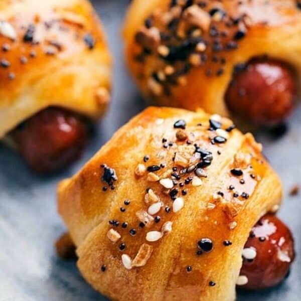 Five pigs in a blanket topped with seasoning are arranged on a gray plate.