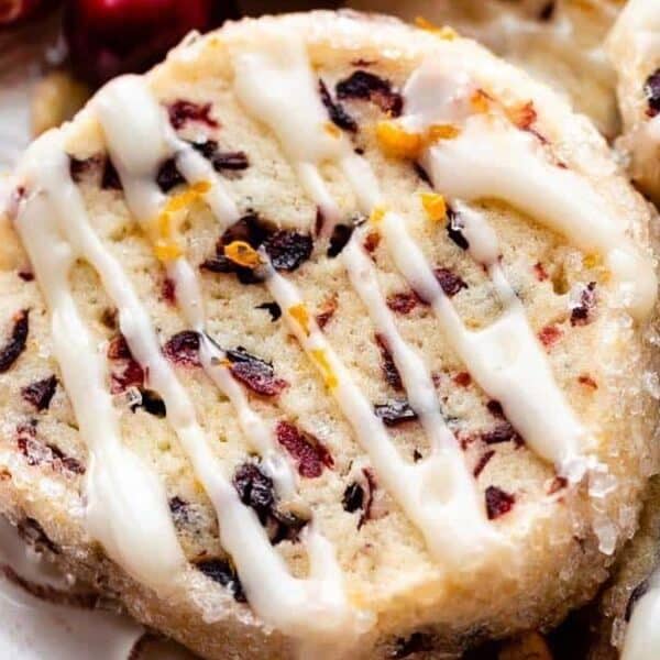 Round cookie topped with dried cranberries, orange zest, and a drizzle of white icing.