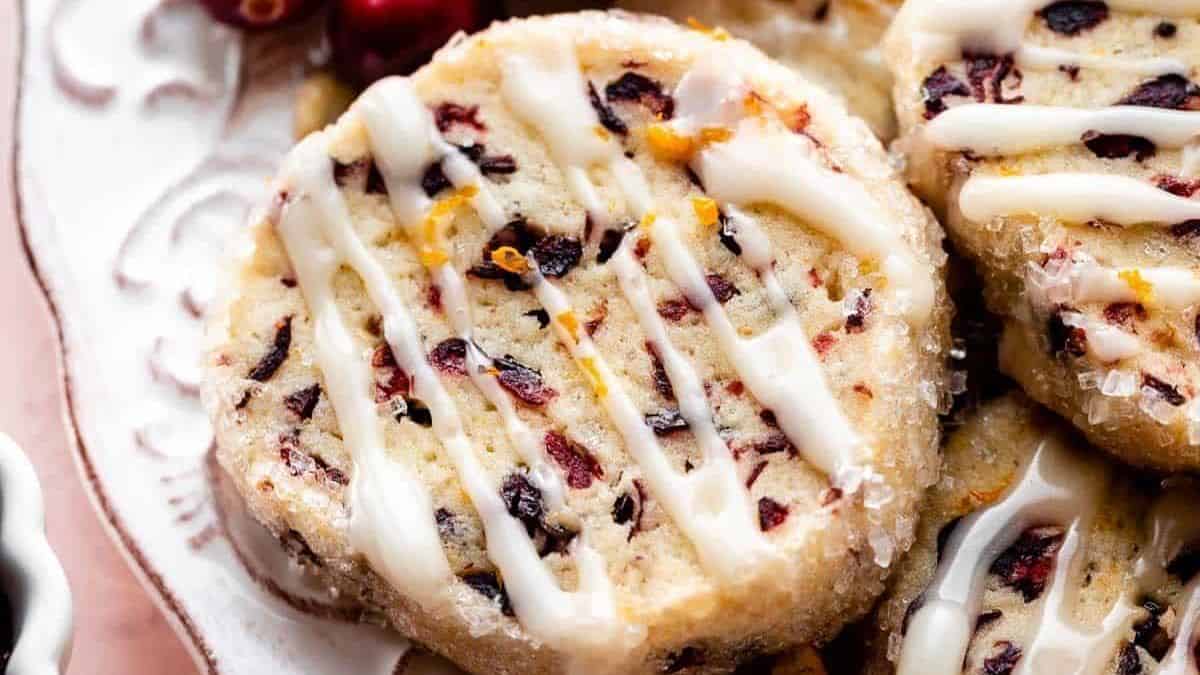 Round cookie topped with dried cranberries, orange zest, and a drizzle of white icing.
