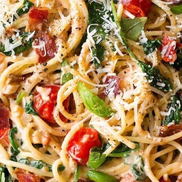 Spaghetti pasta with creamy sauce, cherry tomatoes, spinach, bacon pieces, grated parmesan cheese, and fresh basil on top.