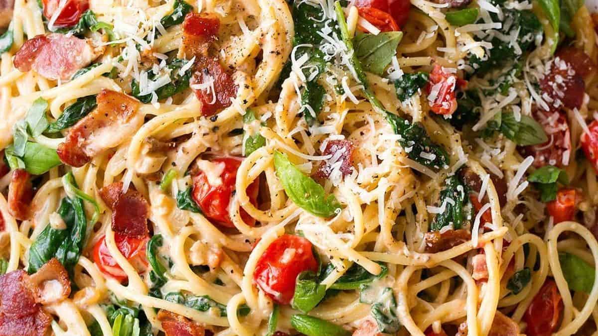 Spaghetti pasta with creamy sauce, cherry tomatoes, spinach, bacon pieces, grated parmesan cheese, and fresh basil on top.