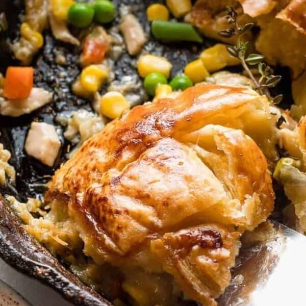 A golden-brown pot pie with flaky crust in a skillet, filled with chicken, peas, carrots, and corn.