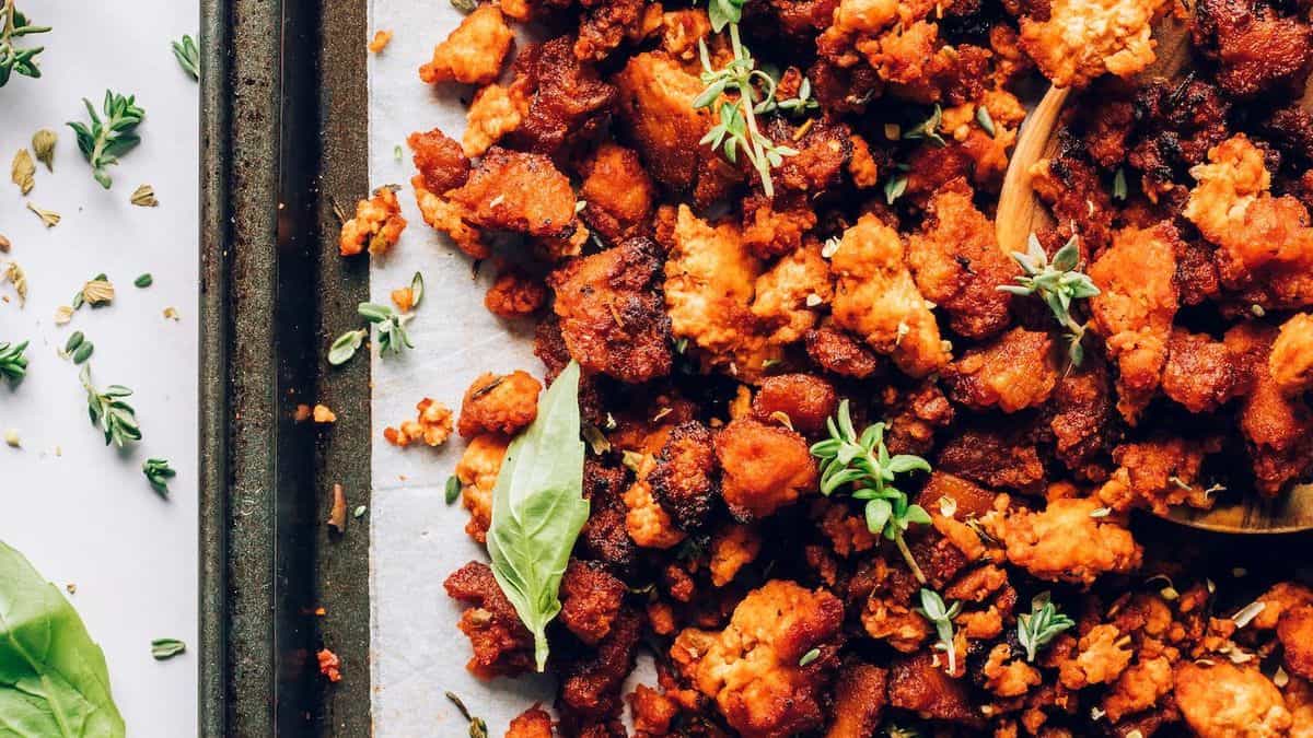 Crumbled, browned tofu mixed with herbs and spices on a baking sheet, fresh basil and thyme garnishes scattered around.