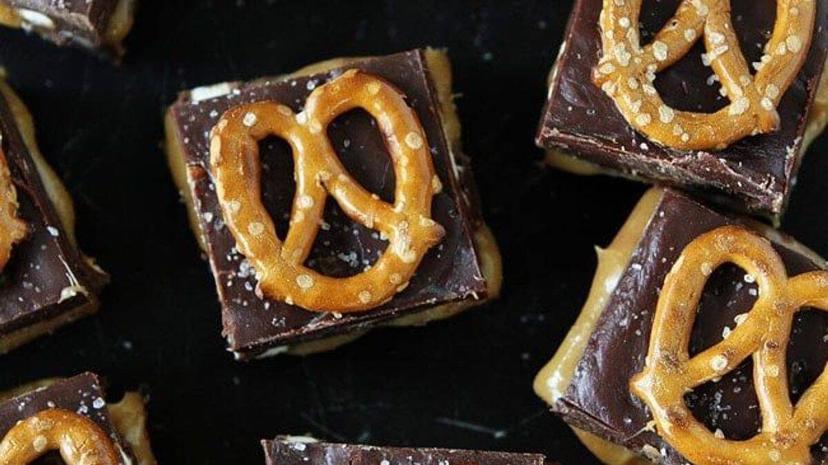 Chocolate and peanut butter bars topped with salted pretzels on a dark surface.