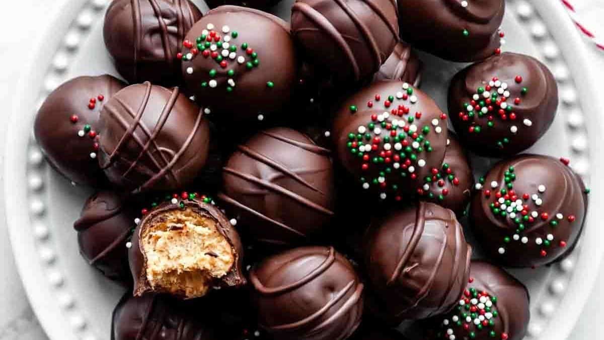 Chocolate-covered truffles on a plate, some with red, white, and green sprinkles; one has a visible peanut butter filling.