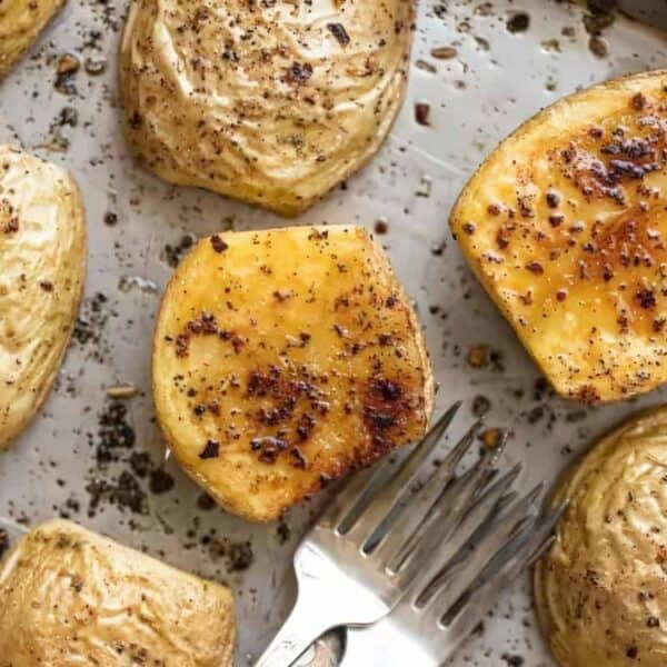 Roasted potato halves with pepper and spices on a baking sheet, a metal fork next to them.