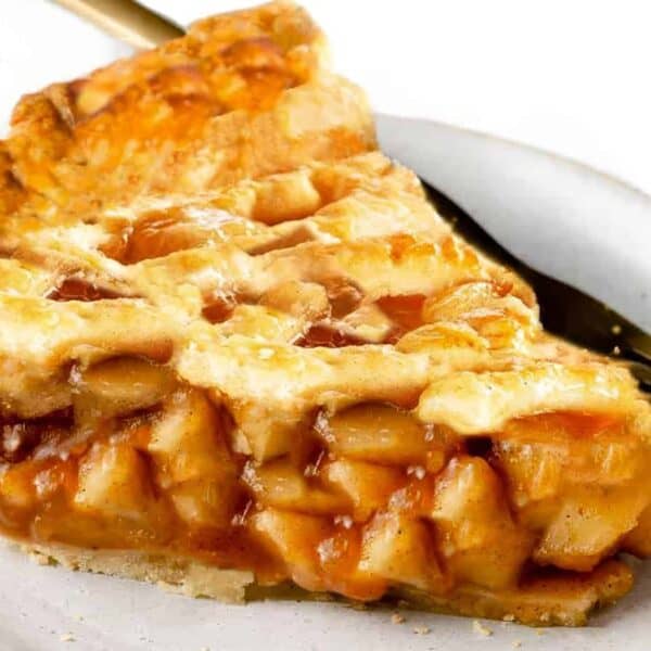 A slice of apple pie with a golden lattice crust on a white plate, with a fork placed next to it.