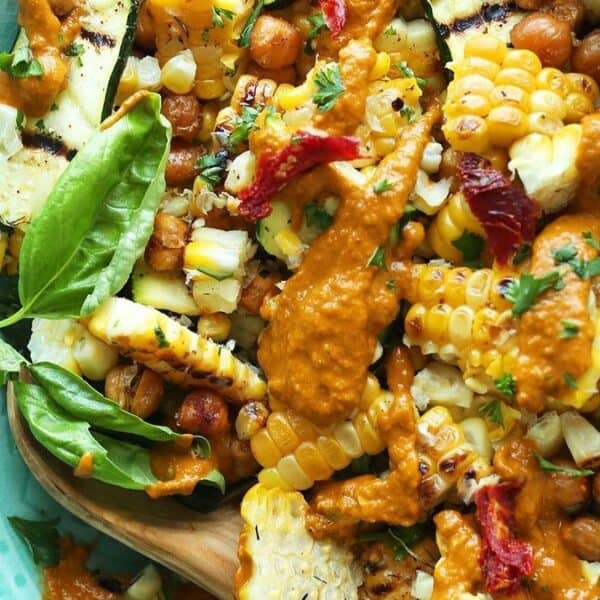 Grilled corn, chickpeas, zucchini, sun-dried tomatoes, basil, and parsley on a plate with creamy orange sauce on top.
