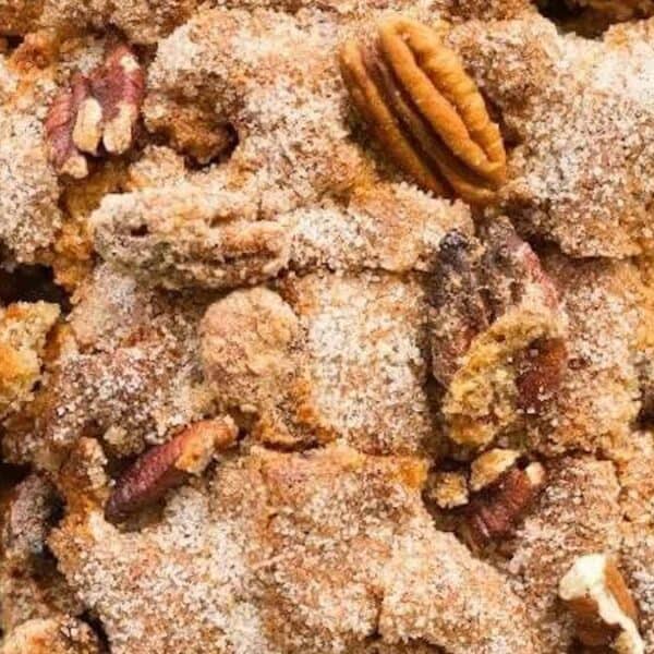 Close-up of baked bread pudding topped with cinnamon sugar and pecans in a parchment-lined baking dish.
