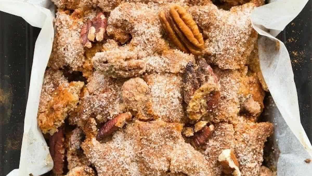 Close-up of baked bread pudding topped with cinnamon sugar and pecans in a parchment-lined baking dish.