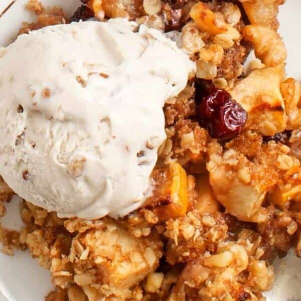 Apple crisp with vanilla ice cream on a white plate, spoon placed beside the dessert.