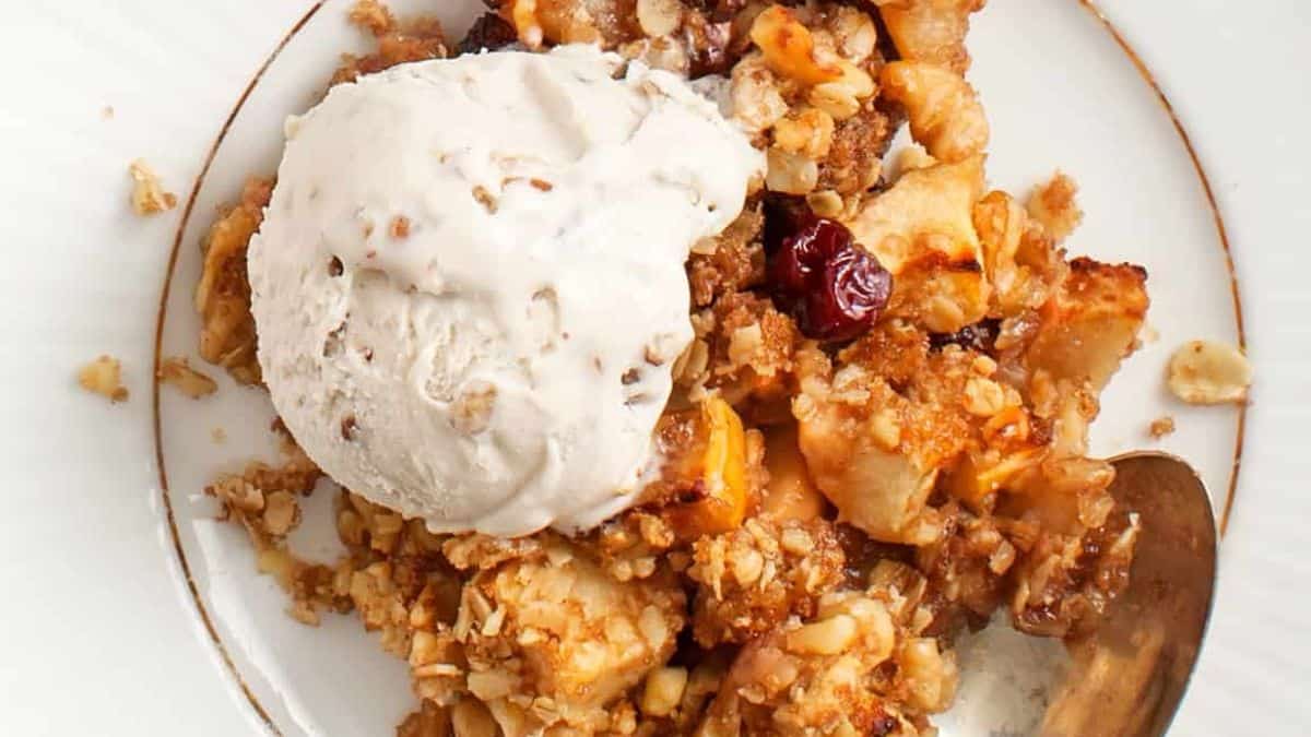 Apple crisp with vanilla ice cream on a white plate, spoon placed beside the dessert.