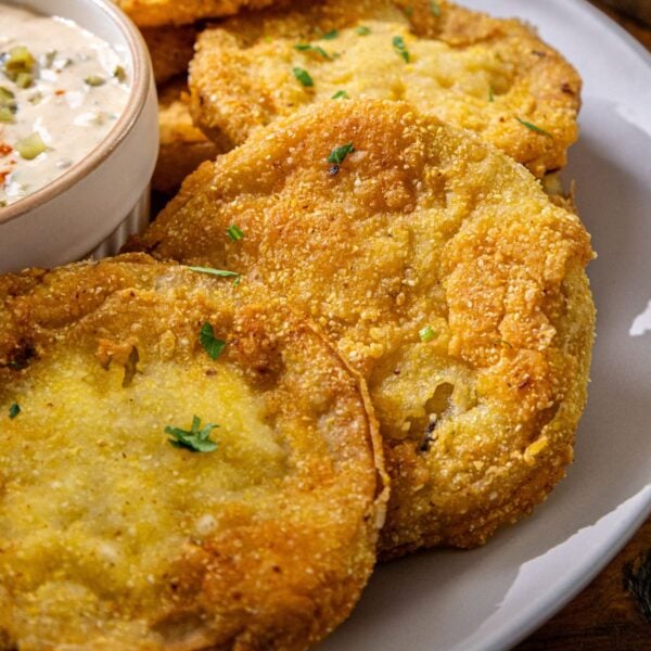 Fried green tomatoes on a white plate with a small bowl of creamy dipping sauce.