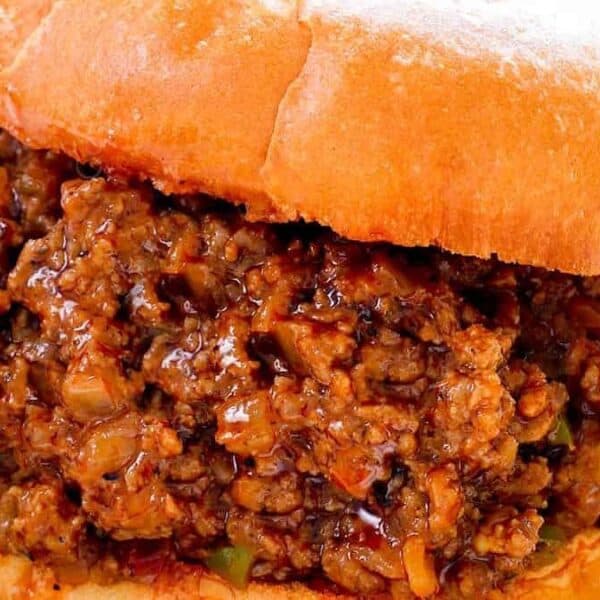 A sloppy joe sandwich with seasoned ground beef in a soft bun sits on a white plate.