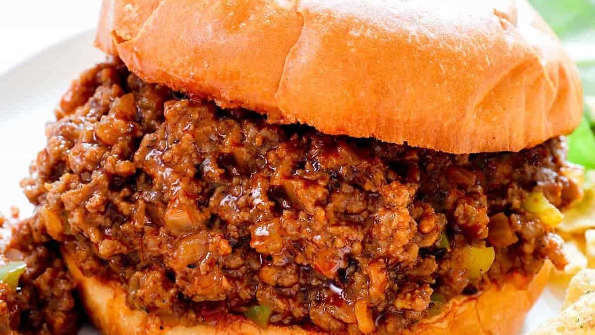 A sloppy joe sandwich with seasoned ground beef in a soft bun sits on a white plate.