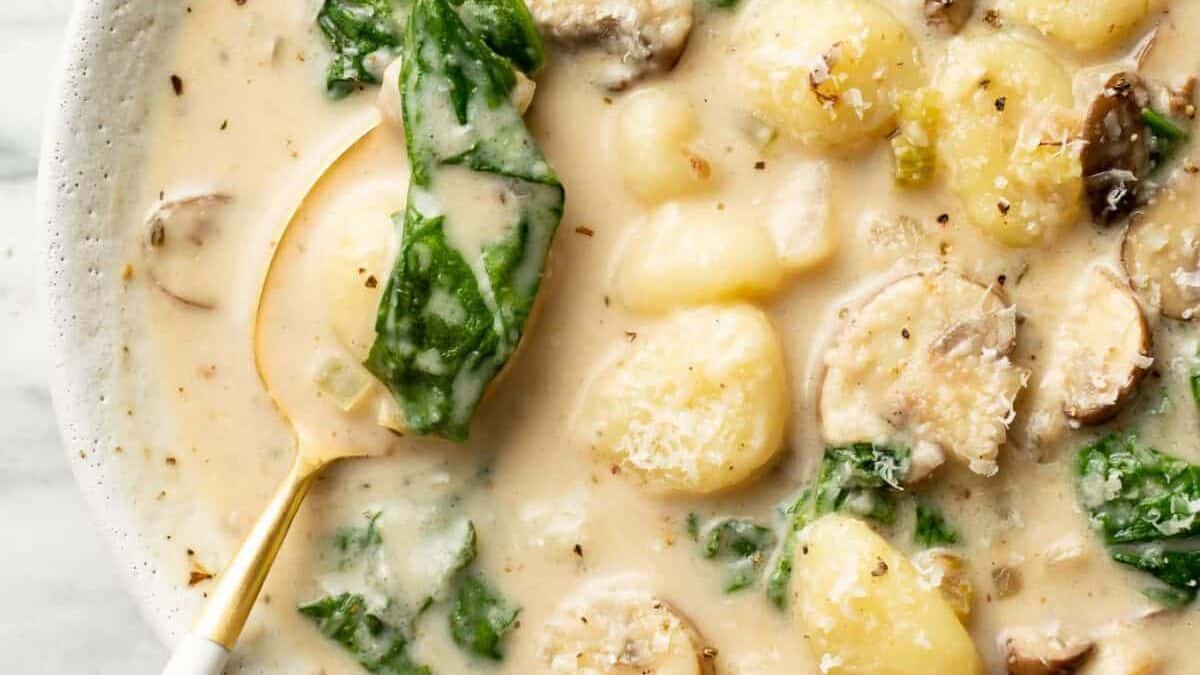 Gnocchi, spinach, and mushrooms in a creamy light broth, served in a white bowl with a ladle.