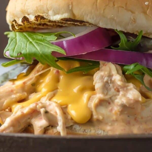 Shredded chicken, melted cheese, leafy greens, and sliced red onions on a sesame seed bun.