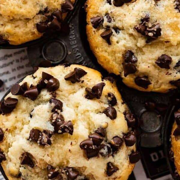 Several chocolate chip muffins in a muffin tin, topped with chocolate chips, placed on newspaper.