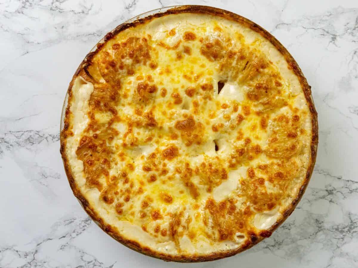 A golden-brown baked pie with a cheesy crust sits on a white marble surface, viewed from above.