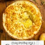 A golden-brown gratin dauphinois topped with melted cheese and herbs on a wooden table.