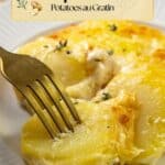 A fork cuts into gratin dauphinois on a white plate, topped with melted cheese and herbs.