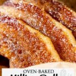 Close-up of three strips of oven-baked candied bacon with a glossy caramelized coating on a white surface.