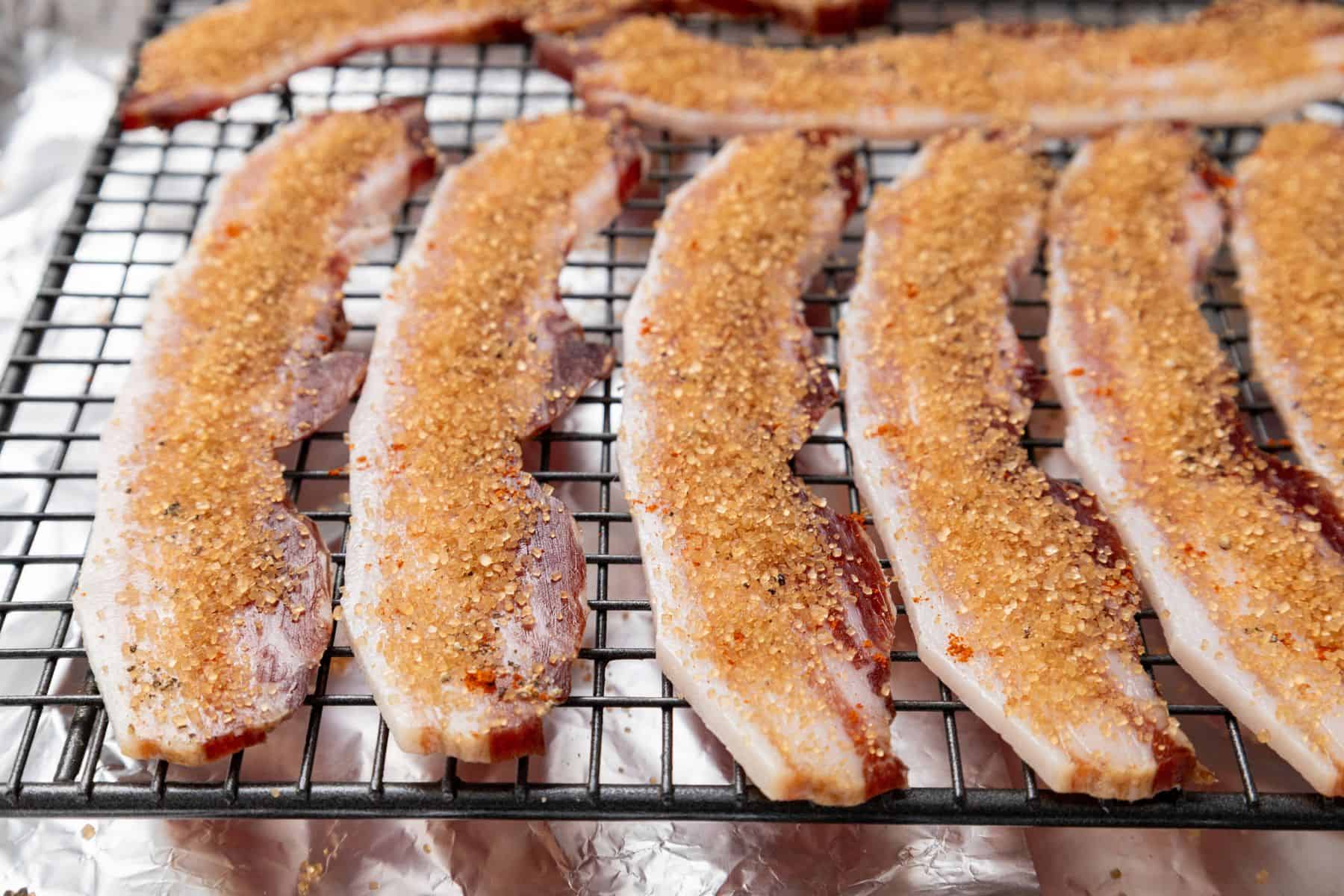 Several strips of raw bacon on a wire rack, sprinkled with brown sugar.