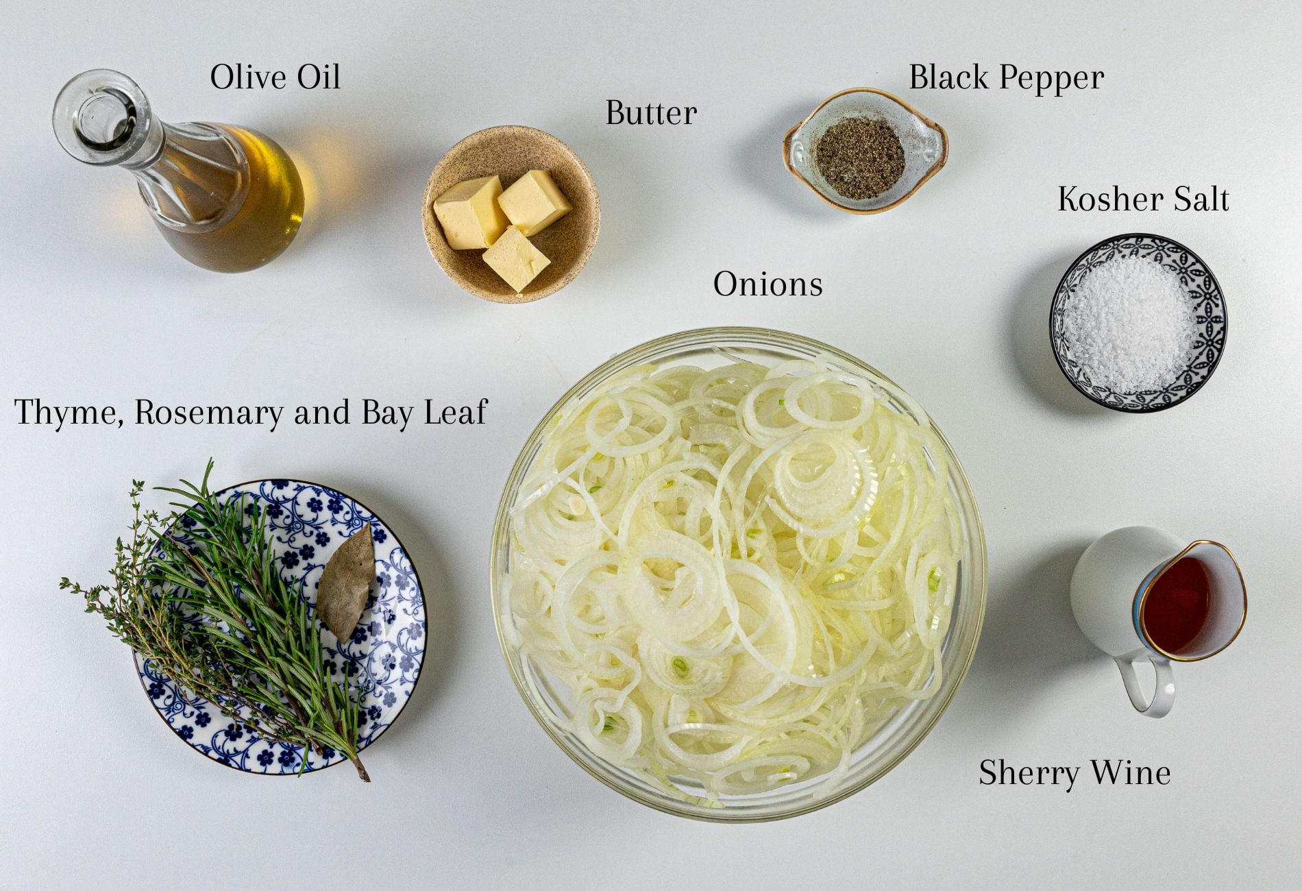 Sliced onions, olive oil, butter, black pepper, kosher salt, thyme, rosemary, bay leaf, and sherry wine arranged top-down.