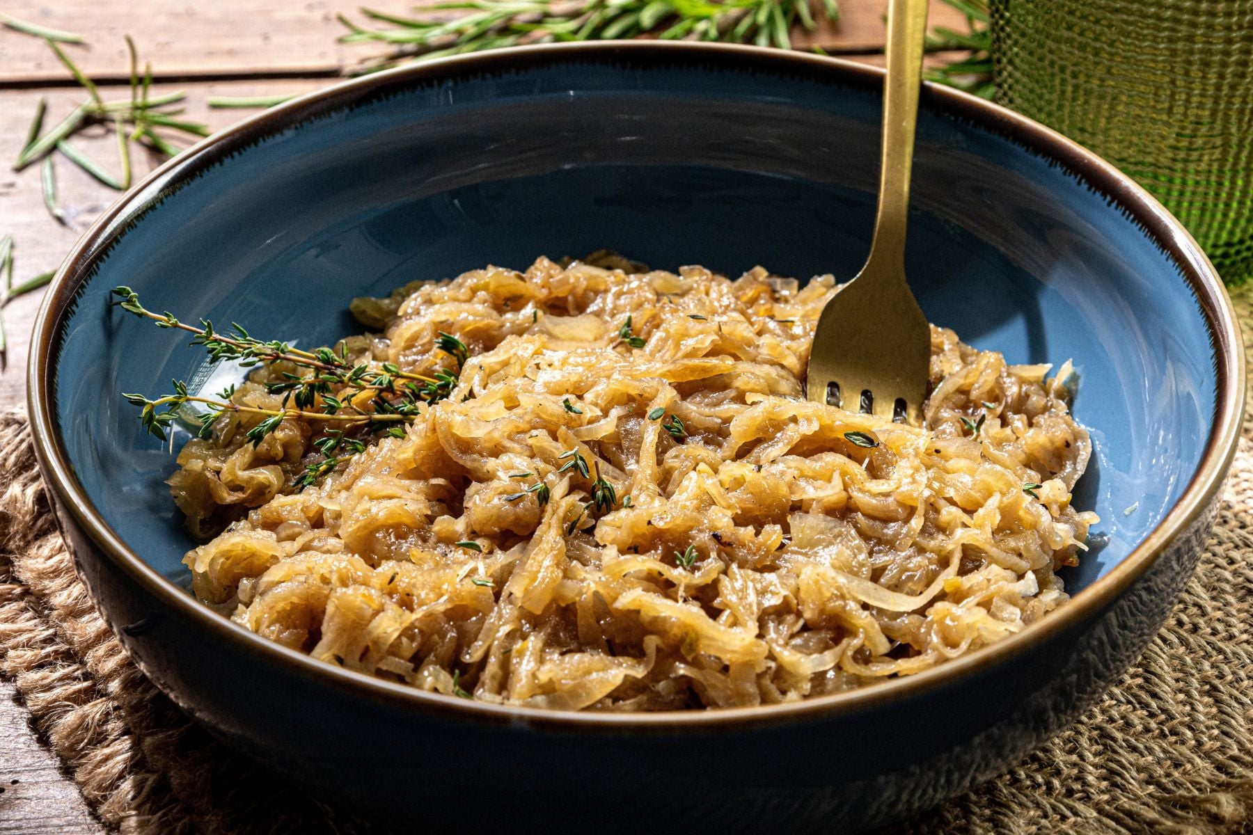 Blue bowl containing caramelized onions and fresh herbs, with a gold fork inside.